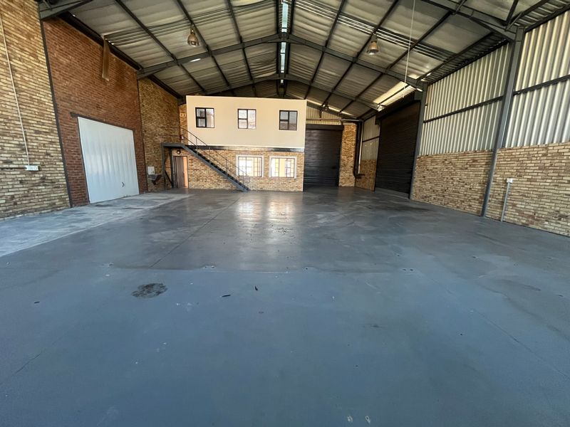 Spacious industrial warehouse featuring high ceilings, exposed brick walls, a mezzanine office level with staircase, and large roller shutter doors for easy access.
