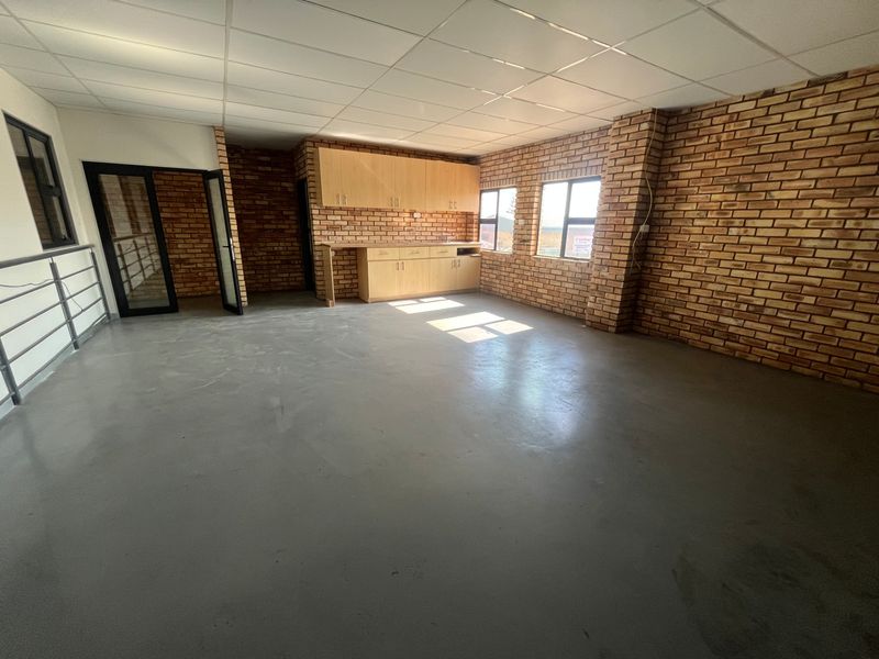 Open-plan industrial office space featuring exposed brick walls, polished concrete flooring, suspended ceiling, and a built-in kitchenette area.