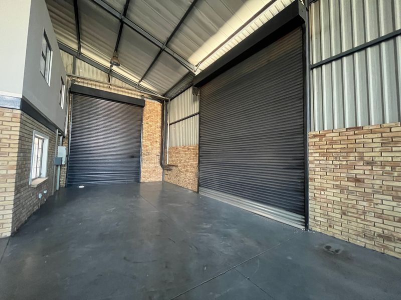 Spacious industrial warehouse unit featuring high ceilings, exposed brickwork, polished concrete flooring, and two large roller shutter doors for easy access.