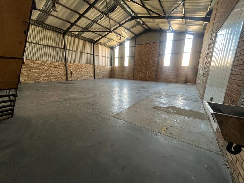 Spacious industrial warehouse featuring high-volume exposed steel truss roofing, face-brick walls, polished concrete flooring, and natural light through vertical windows.