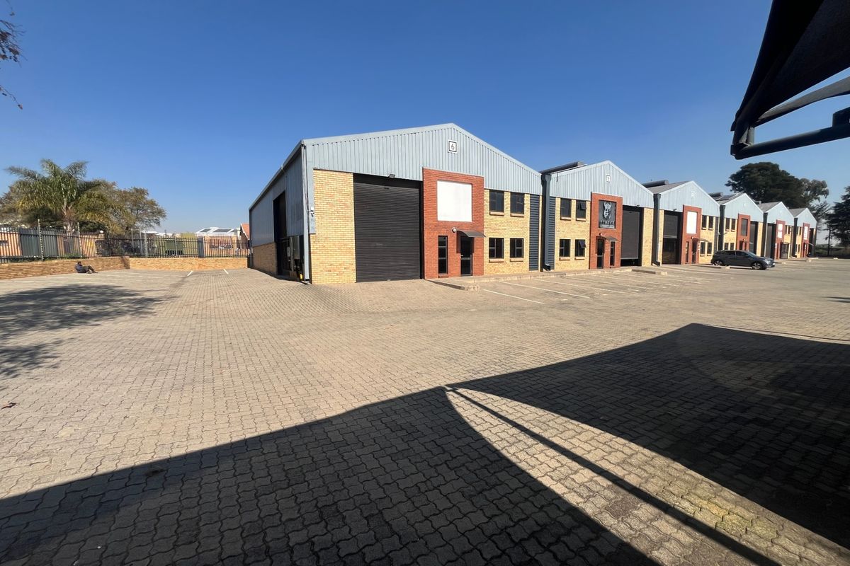 Exterior view of a multi-unit industrial complex featuring brick and metal cladding, roller shutter doors, and a paved parking area.