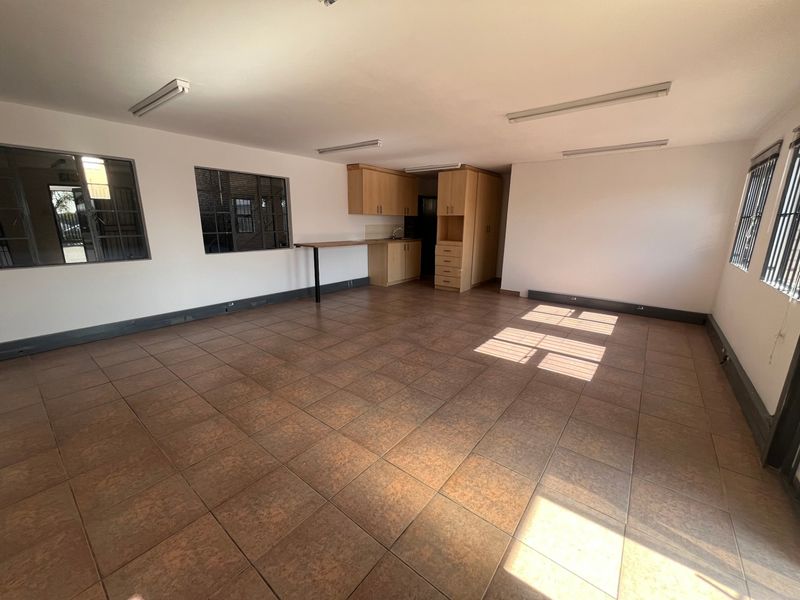 Open plan industrial office or utility space featuring tiled flooring, built-in kitchenette cabinetry, and security-barred windows.