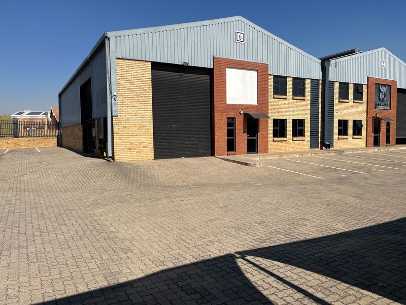 Industrial warehouse unit featuring a large roller shutter door, brick and metal cladding facade, and dedicated paved parking area.