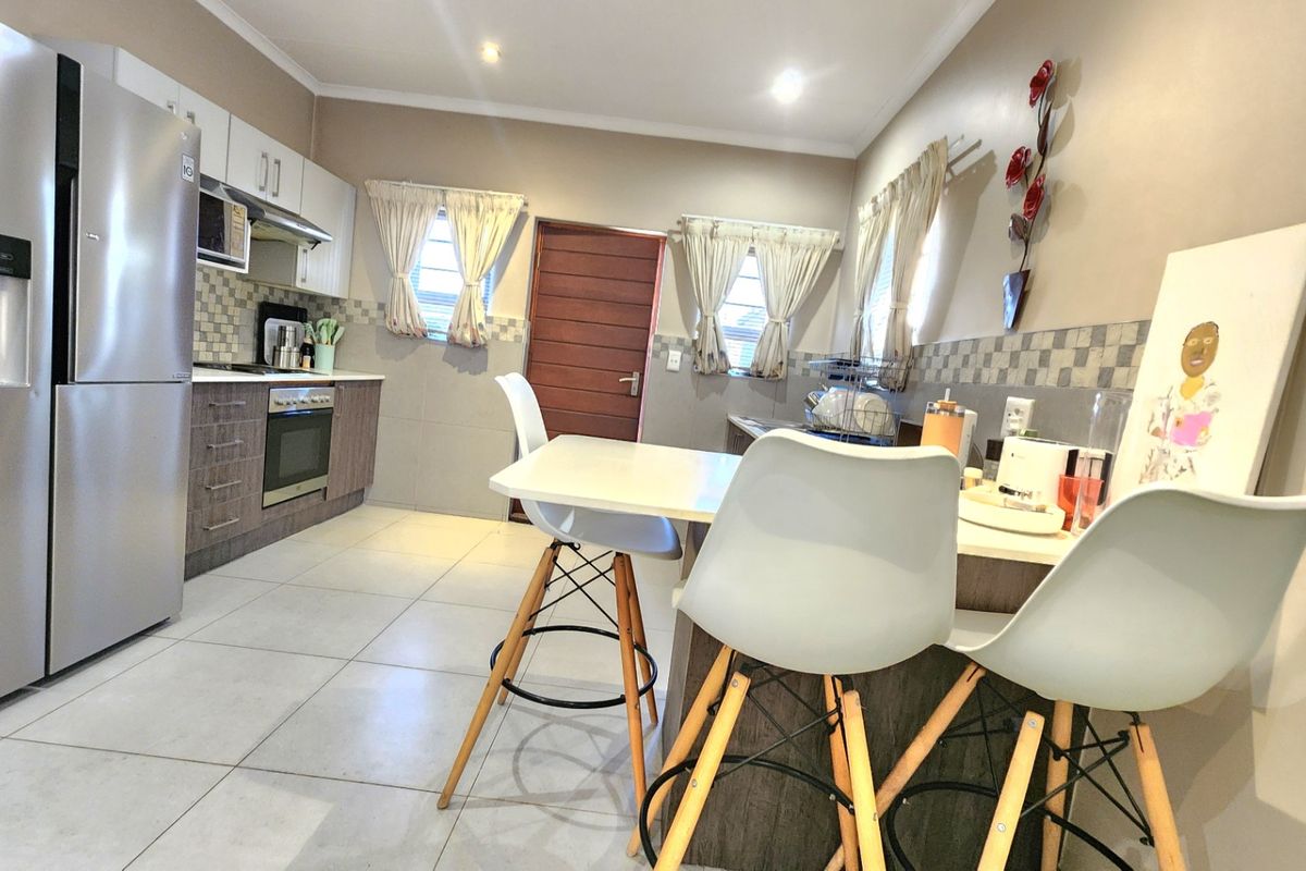 Modern kitchen featuring built-in cabinetry, tiled backsplash, integrated oven and hob, and a breakfast nook area with tiled flooring.