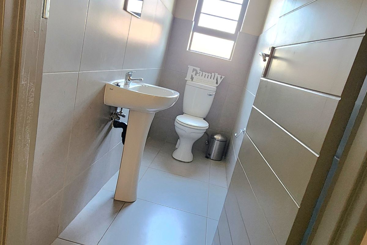 A clean and functional guest bathroom featuring a pedestal basin, a standard toilet, and neutral wall and floor tiling.