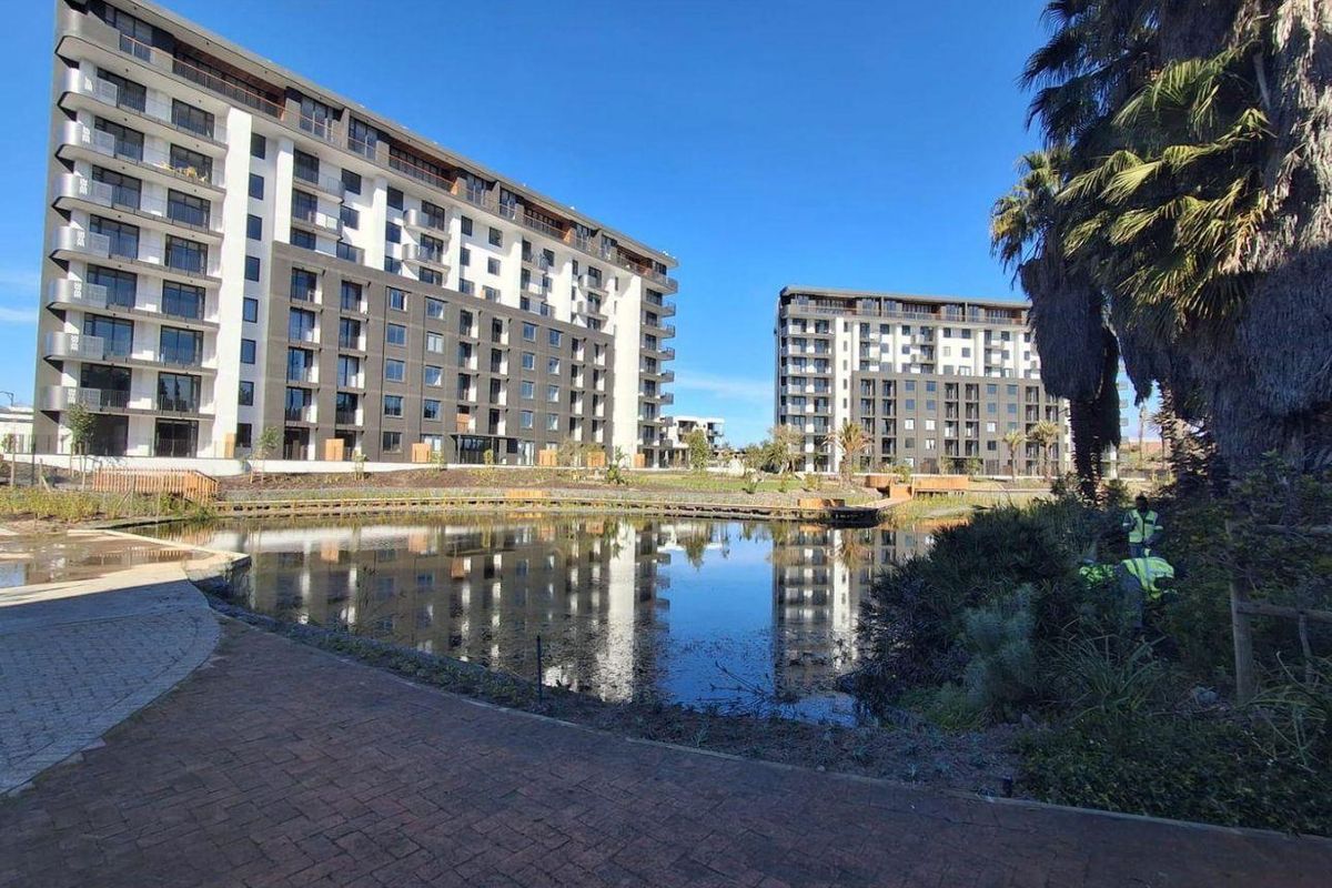 Exterior view of modern multi-story apartment buildings overlooking a landscaped pond and paved communal walkways.