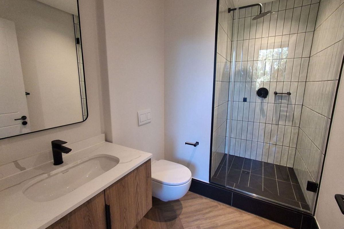 Modern bathroom featuring a walk-in shower with black fixtures, wall-mounted toilet, and a sleek vanity with stone countertop and herringbone flooring.