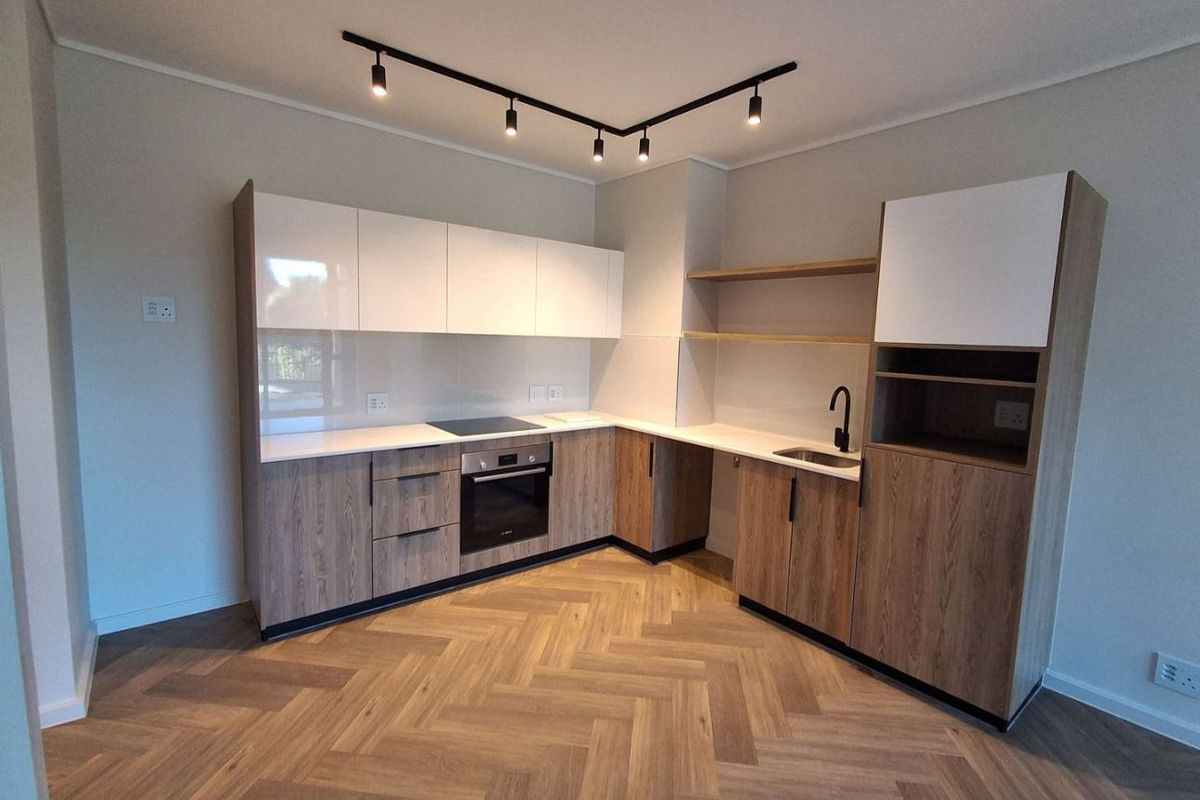 Modern kitchen featuring two-tone cabinetry, integrated appliances, sleek black fixtures, and stylish herringbone wood flooring in an open-plan layout.