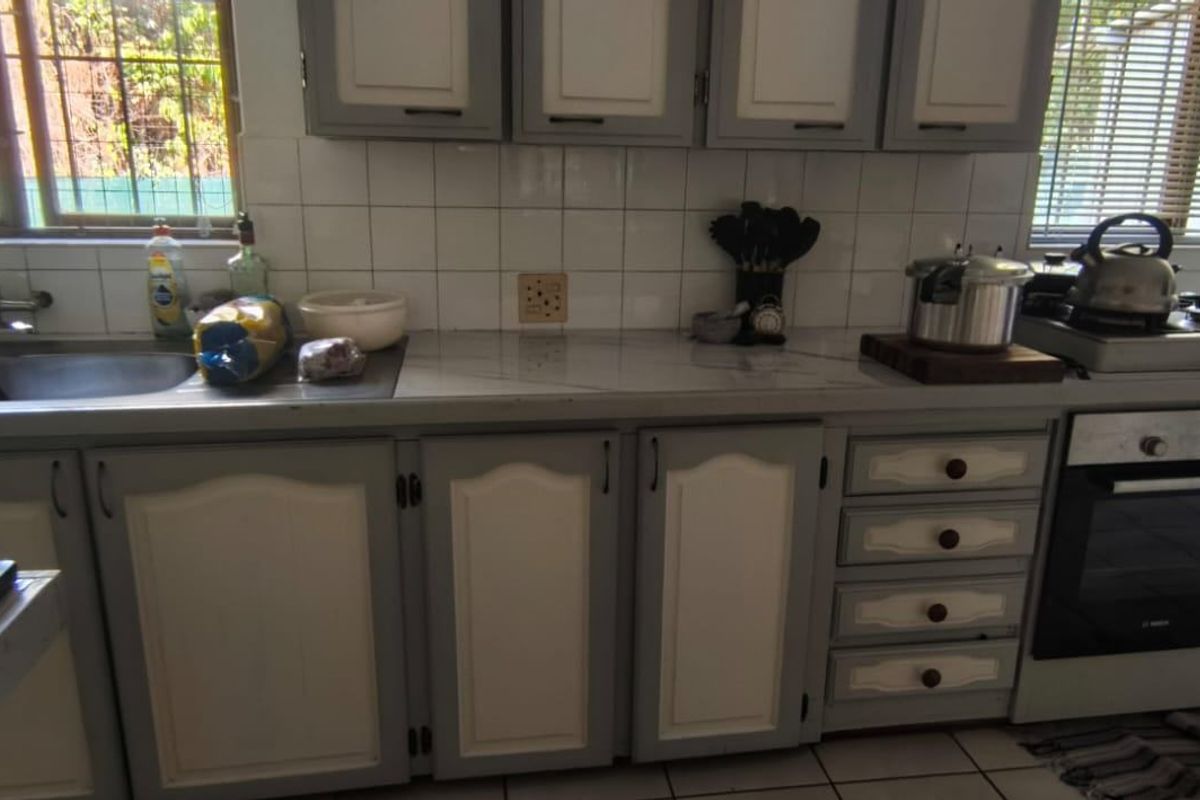A functional kitchen featuring two-tone cabinetry, a built-in oven, gas hob, and a stainless steel double sink with tiled backsplash.