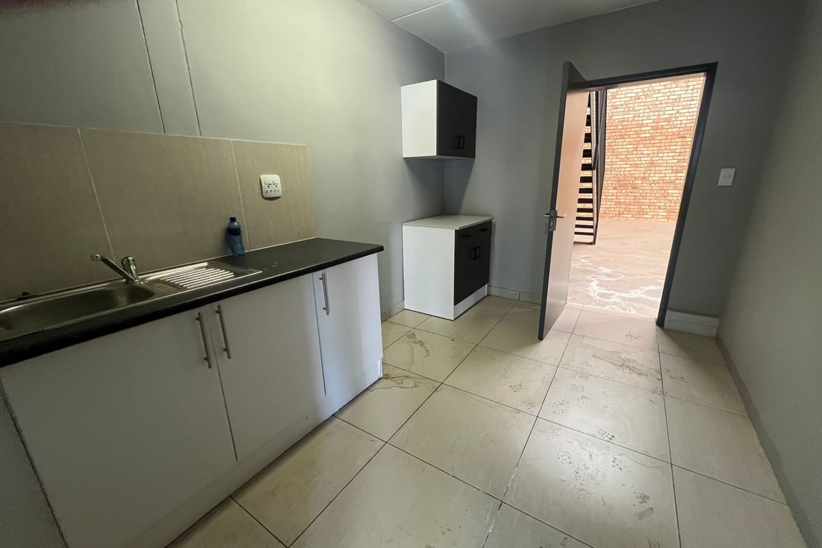 A functional kitchenette area featuring built-in cabinetry, a stainless steel sink, and tiled flooring, with direct access to an outdoor area.