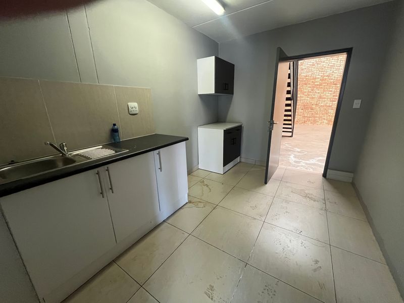 A functional kitchenette area featuring built-in cabinetry, a stainless steel sink, and tiled flooring, with direct access to an outdoor area.