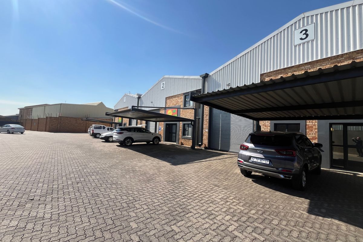 Exterior view of an industrial complex featuring multiple units with brick facades, corrugated metal roofing, and individual covered parking bays.