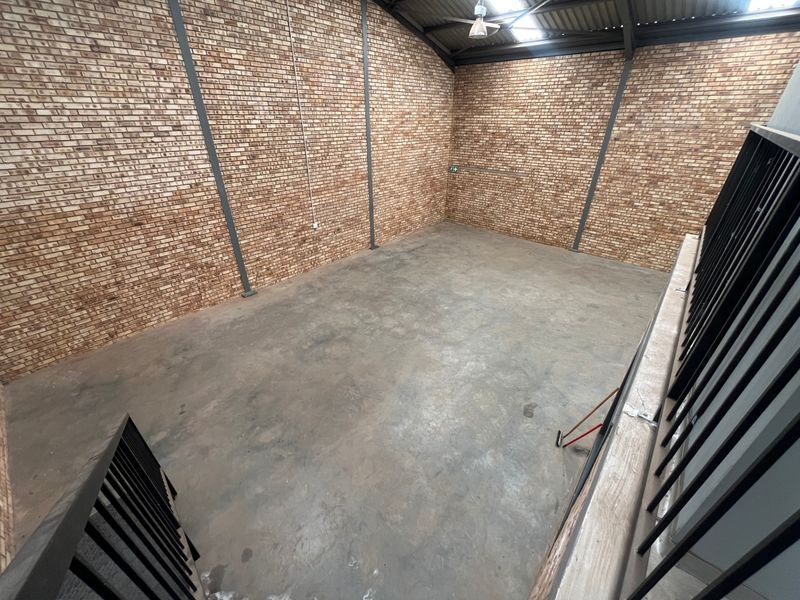 Spacious industrial mezzanine area featuring exposed brick walls, steel structural supports, and a durable concrete floor.