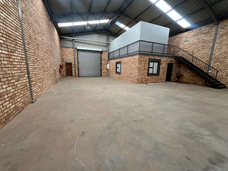 Spacious industrial warehouse unit featuring exposed brick walls, a high-clearance roller shutter door, and a mezzanine level with integrated staircase.