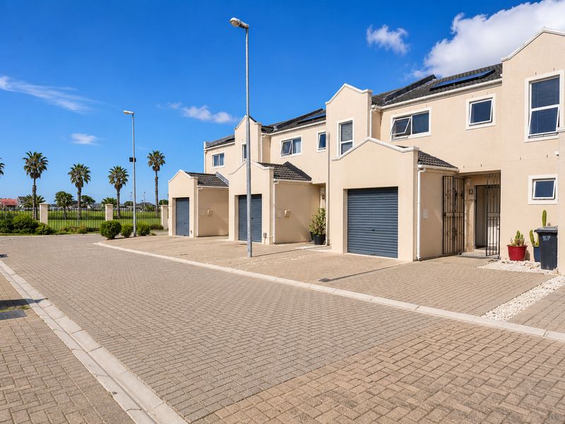 Exterior view of a modern townhouse complex featuring paved driveways, individual garage doors, and secure gated entrances under a clear blue sky.