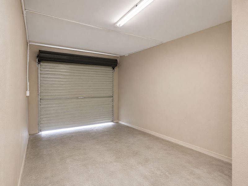 A clean and well-maintained single garage featuring a roller shutter door, concrete flooring, and functional overhead lighting.