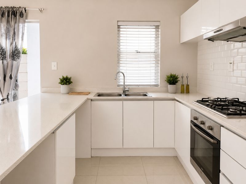 Modern kitchen featuring white cabinetry, stone countertops, a stainless steel gas hob, built-in oven, and a double sink with a window view.
