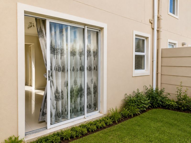 Rear view of the townhouse featuring a sliding glass door leading to a small garden area with manicured lawn and perimeter wall.