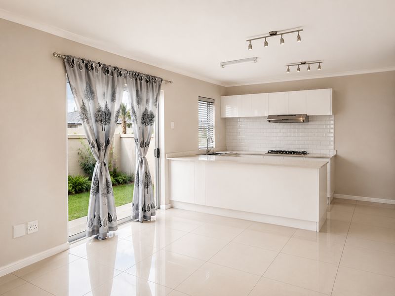 Modern open-plan kitchen featuring white cabinetry, stone countertops, subway tile backsplash, and integrated gas hob, flowing seamlessly to an outdoor patio area.