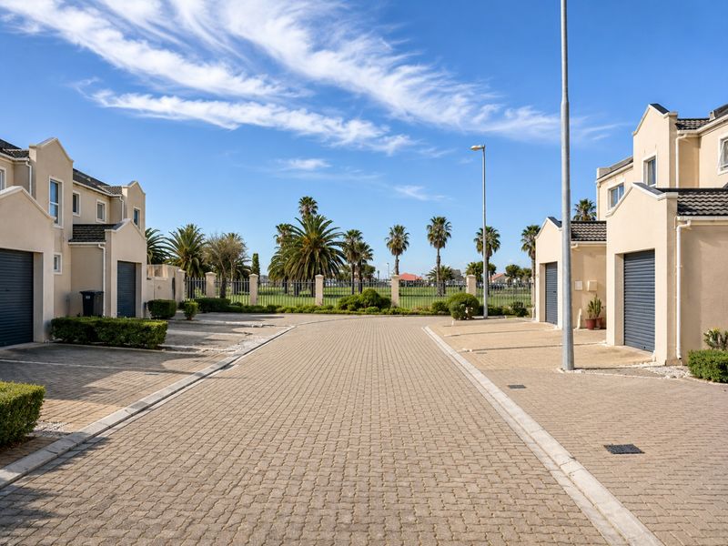 A view of the paved driveway and entrance area of a townhouse complex, featuring multiple garage doors and landscaped surroundings.