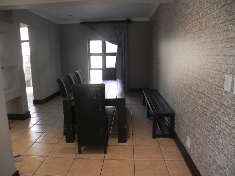 A dining room featuring tiled flooring and a textured brick feature wall, providing a functional space for family meals.