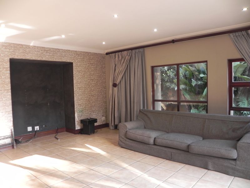 A living room featuring tiled flooring, recessed media wall with brick-effect cladding, and large windows with curtain tracks.
