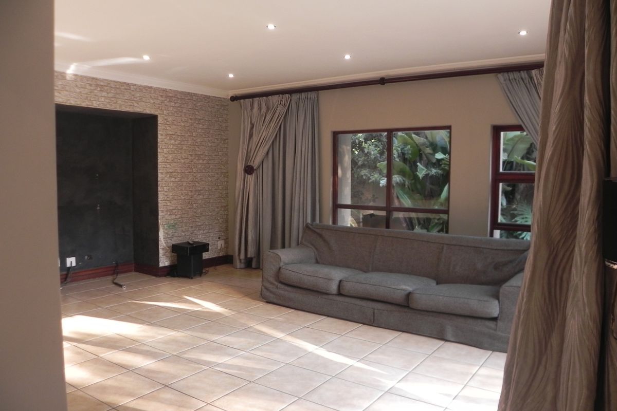 Spacious living room featuring tiled flooring, recessed ceiling lighting, and a textured brick-style feature wall with a dedicated media alcove.