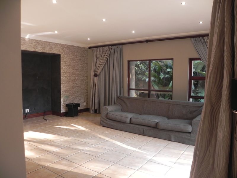 Spacious living room featuring tiled flooring, recessed ceiling lighting, and a textured brick-style feature wall with a dedicated media alcove.