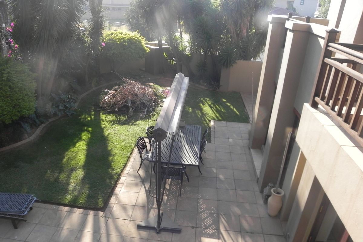 An elevated view of a paved patio area and garden, featuring a multi-level building facade and mature landscaping.