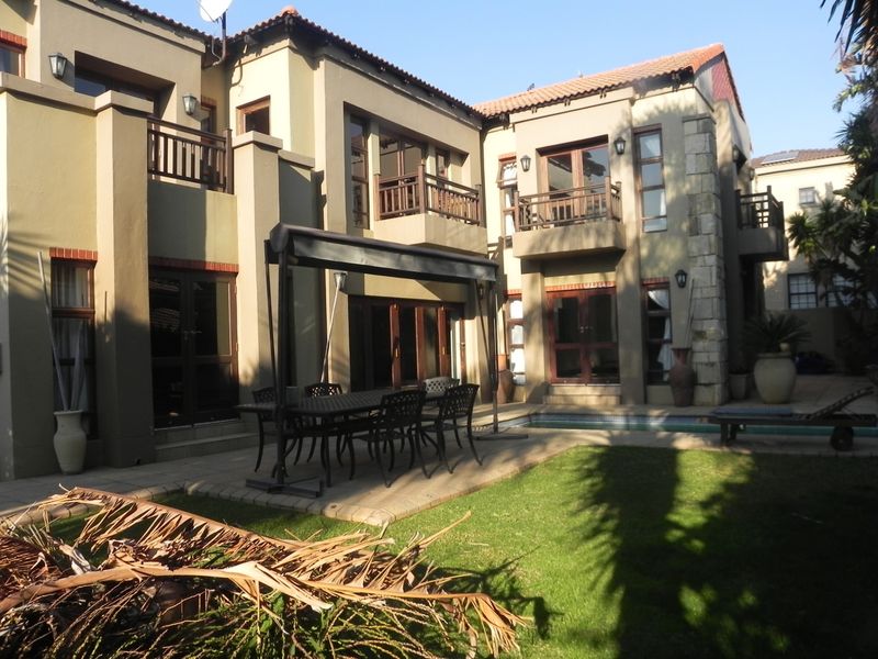 Rear view of a multi-story residence featuring a paved patio area, swimming pool, landscaped garden, and multiple balconies with timber railings.
