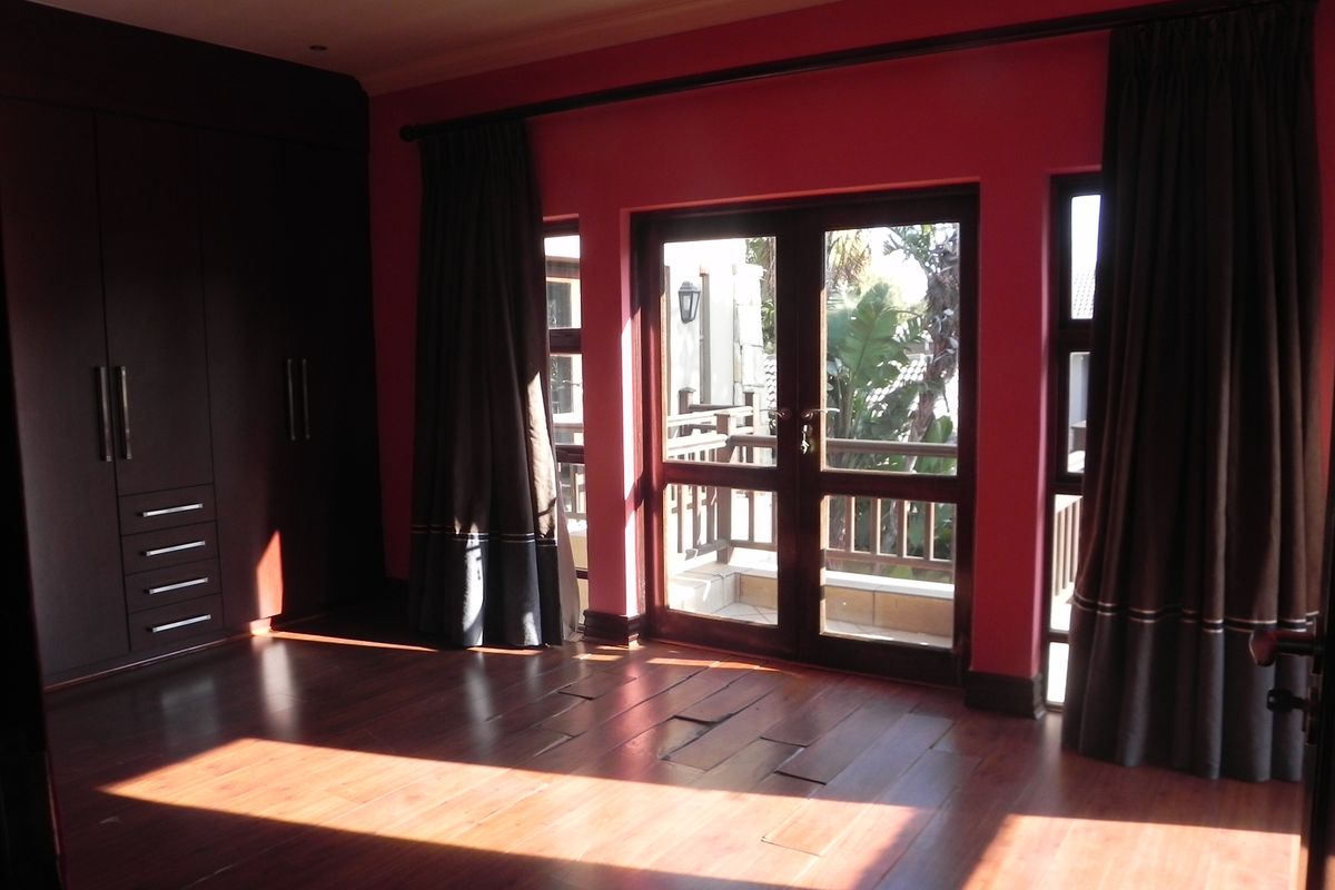 Spacious bedroom featuring dark built-in cabinetry, timber flooring, and double doors opening onto a private balcony.