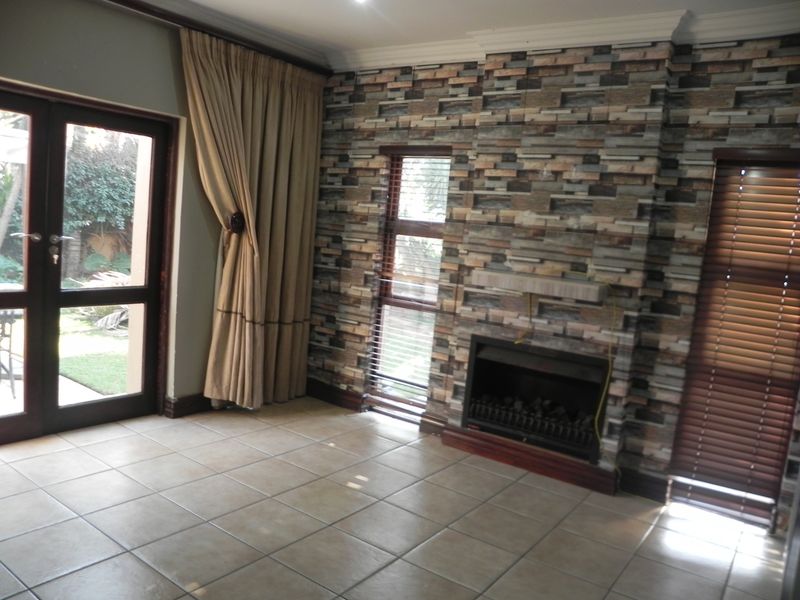 Living room featuring tiled flooring, a built-in fireplace with decorative stone-effect cladding, and double doors providing access to the garden.