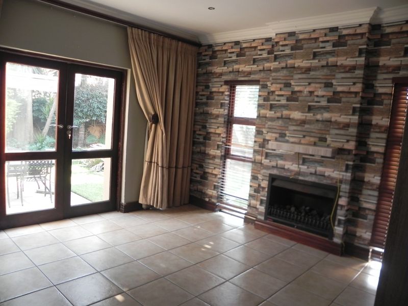 Living room featuring a built-in fireplace with decorative stone-effect cladding, tiled flooring, and double doors providing direct access to the outdoor patio area.