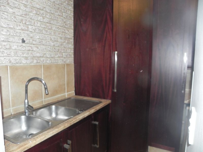 A functional scullery area featuring dark wood cabinetry, a double stainless steel sink, and a textured brick feature wall.