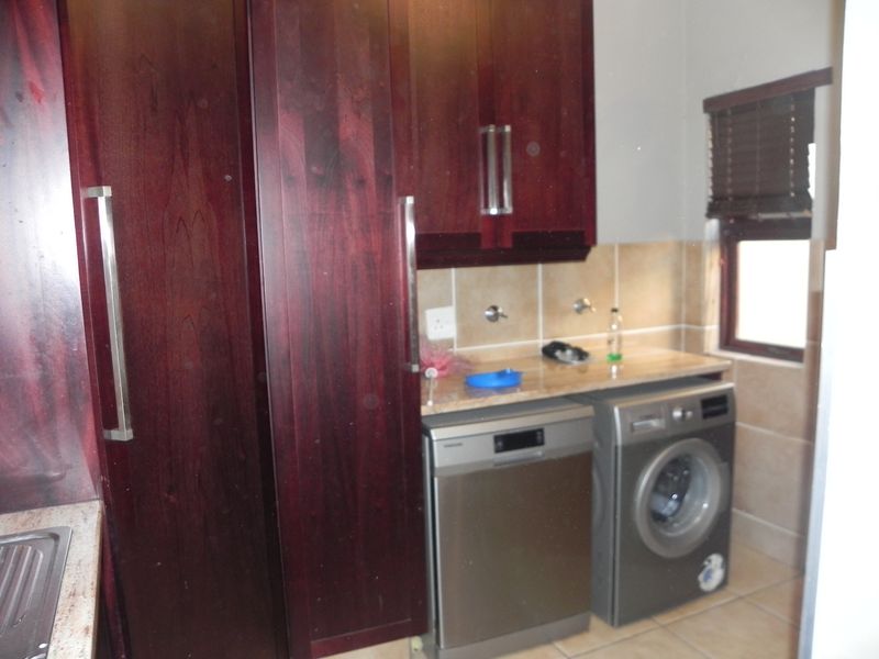 A functional laundry area featuring dark wood cabinetry, stone-look countertops, tiled splashbacks, and dedicated spaces for a dishwasher and washing machine.