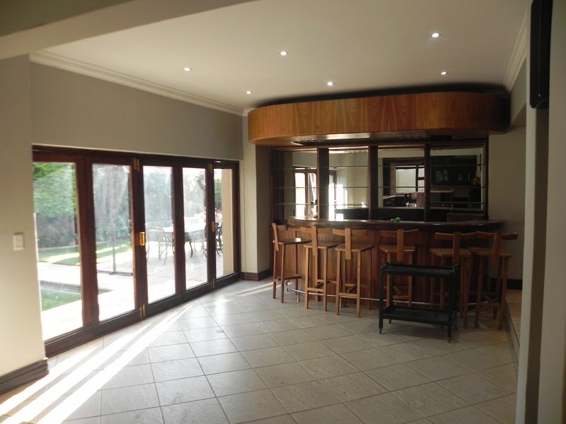 A spacious entertainment area featuring a built-in wooden bar with shelving and large folding glass doors opening to the outdoor patio.