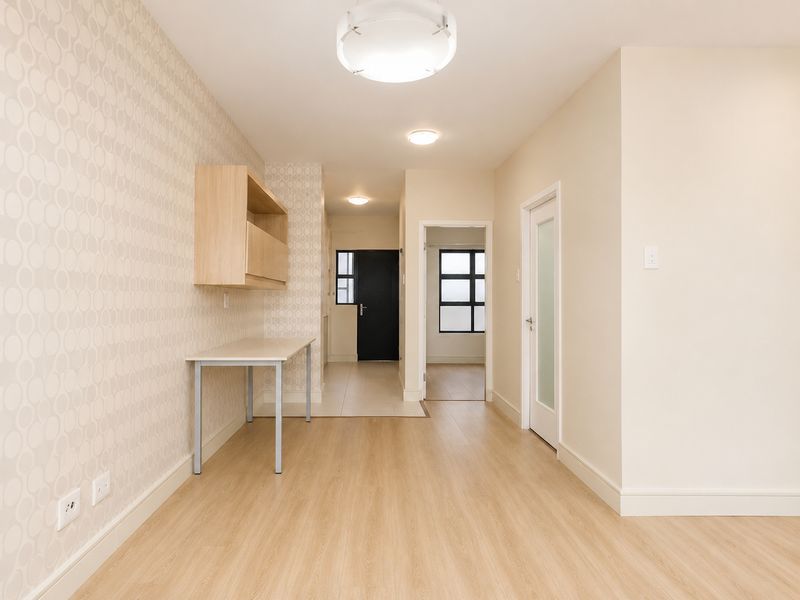A bright hallway featuring light wood-look flooring, patterned wallpaper, a built-in desk unit, and access to adjacent rooms through modern interior doors.