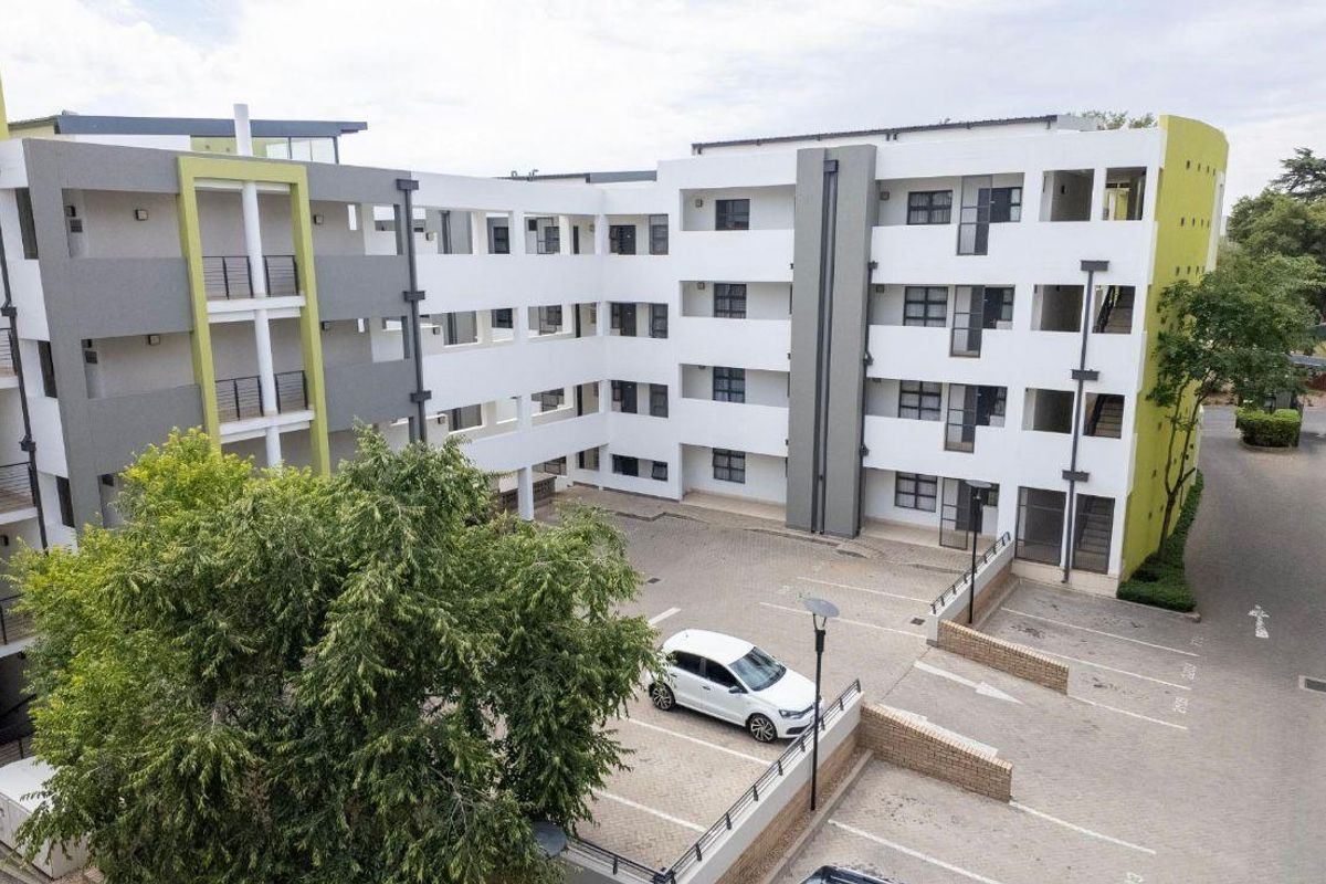 Aerial view of a modern multi-story apartment complex featuring a paved courtyard, designated parking bays, and contemporary architectural facade.