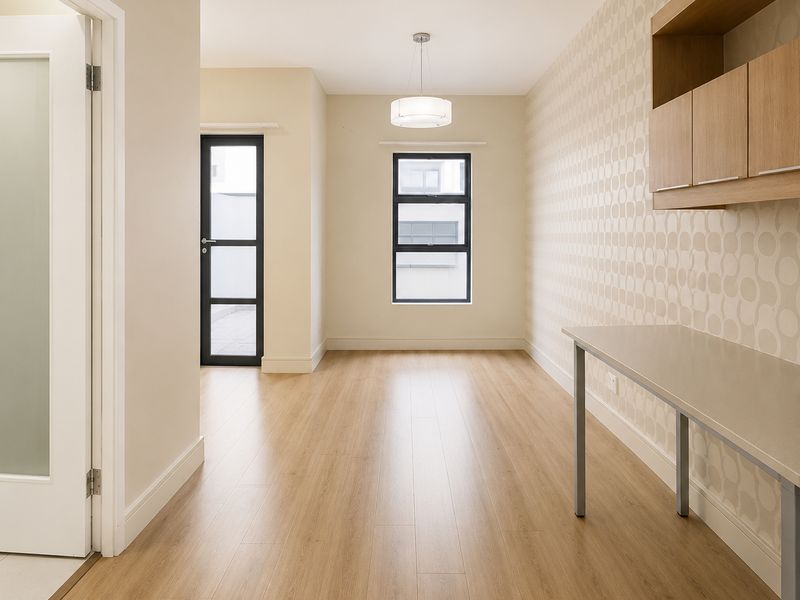 A bright, modern office space featuring light wood-look flooring, built-in wall cabinetry, a desk surface, and a glass-paneled door leading to an outdoor area.