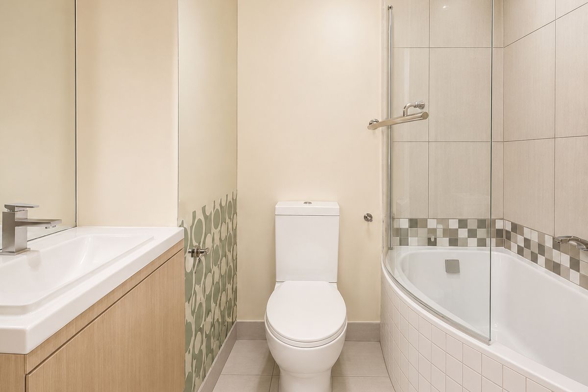 A modern bathroom featuring a vanity with integrated basin, a toilet, and a shower-over-bath combination with a glass screen.