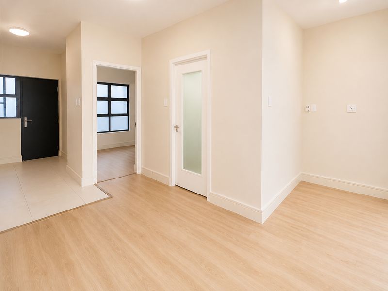 A bright, modern hallway featuring light wood-look flooring, neutral walls, and a frosted glass interior door leading to an adjacent room.