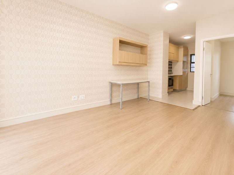 Open-plan living area featuring light wood-look flooring, patterned wallpaper, and a compact kitchen with built-in cabinetry and integrated appliances.