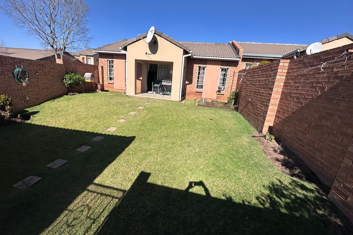 A private rear garden featuring a level lawn, brick boundary walls, and a covered patio area attached to the townhouse.
