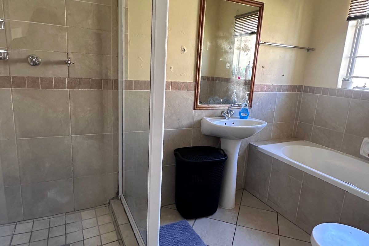 A functional bathroom featuring a separate shower enclosure, bathtub, pedestal basin, and toilet, with tiled finishes throughout.