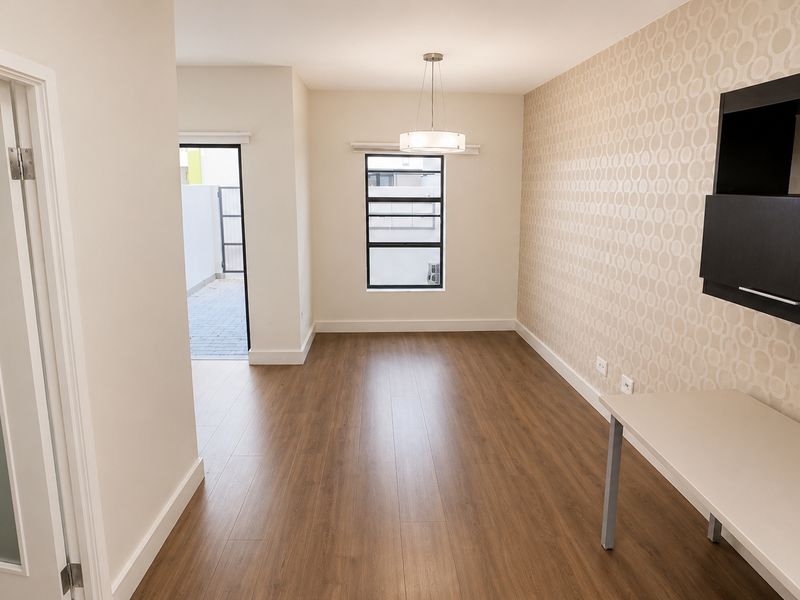 A bright, modern office space featuring wood-look flooring, patterned wallpaper, a built-in desk unit, and direct access to an outdoor patio area.