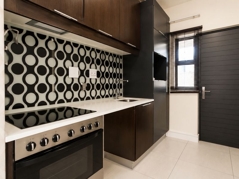 Modern kitchen featuring dark wood cabinetry, a patterned backsplash, integrated oven and hob, and sleek tiled flooring.