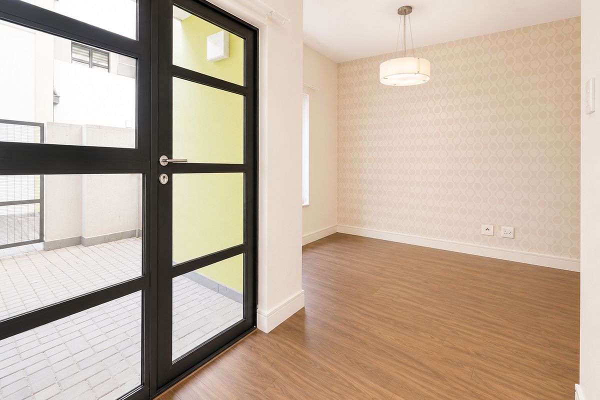 Bright living area featuring wood-look flooring, patterned wallpaper, and a modern glass-paneled door providing direct access to a private paved patio.