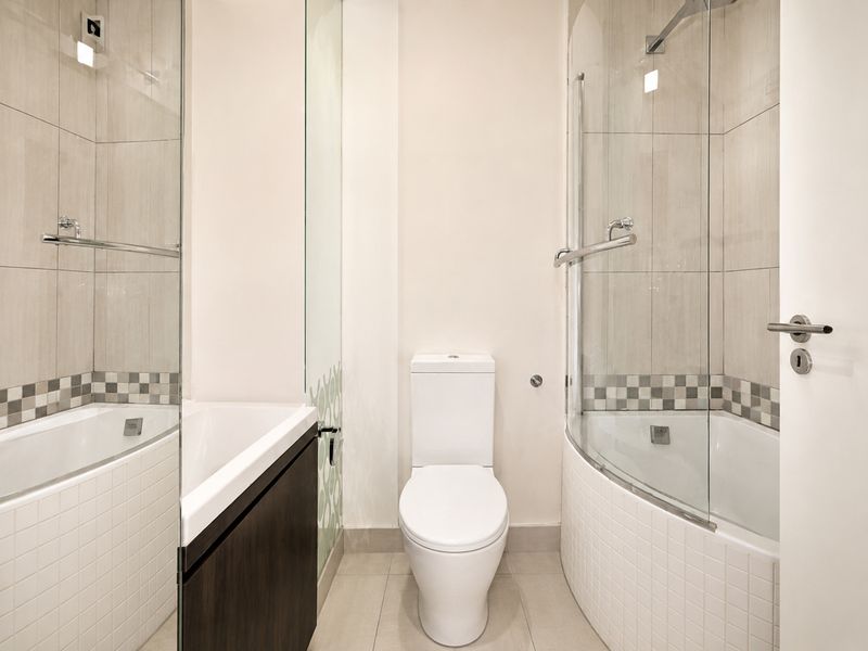 Modern bathroom featuring a white toilet, a curved glass shower enclosure, and a built-in vanity unit with neutral wall and floor tiling.