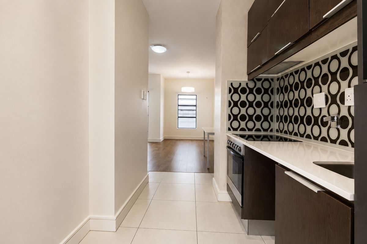 A modern kitchen featuring dark cabinetry, white countertops, and a patterned backsplash, leading into an open-plan living area with hardwood flooring.