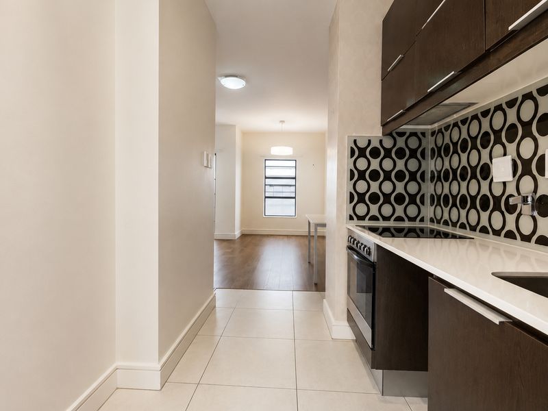 A modern kitchen featuring dark cabinetry, white countertops, and a patterned backsplash, leading into an open-plan living area with hardwood flooring.